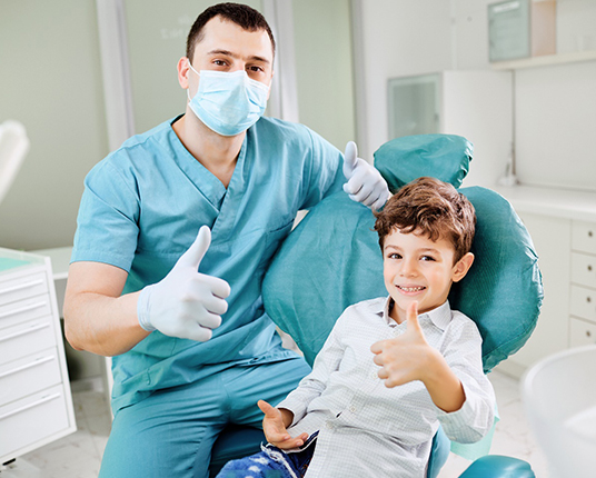 Child and pediatric dentist giving thumbs up at dental checkup