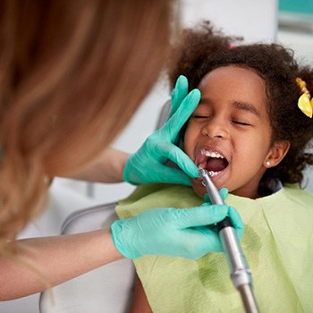 Dental hygienist cleaning child's teeth at routine checkup