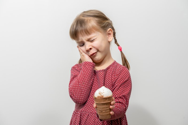 Child holding her cheek eating ice cream due to cavities