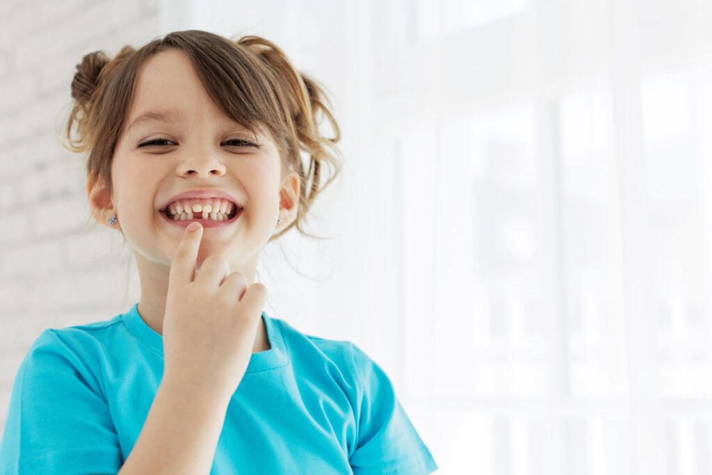 Little girl pointing to gap in grin from lost baby tooth